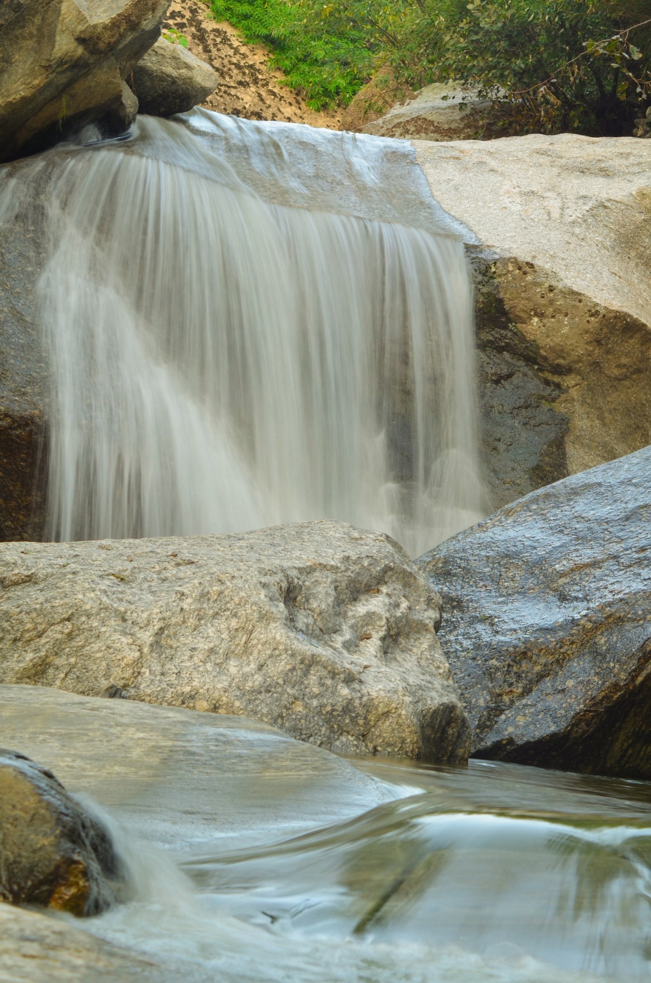 Free Landscapes photos. Serene waterfall flowing over smooth rocks, surrounded by lush greenery and natural beauty.